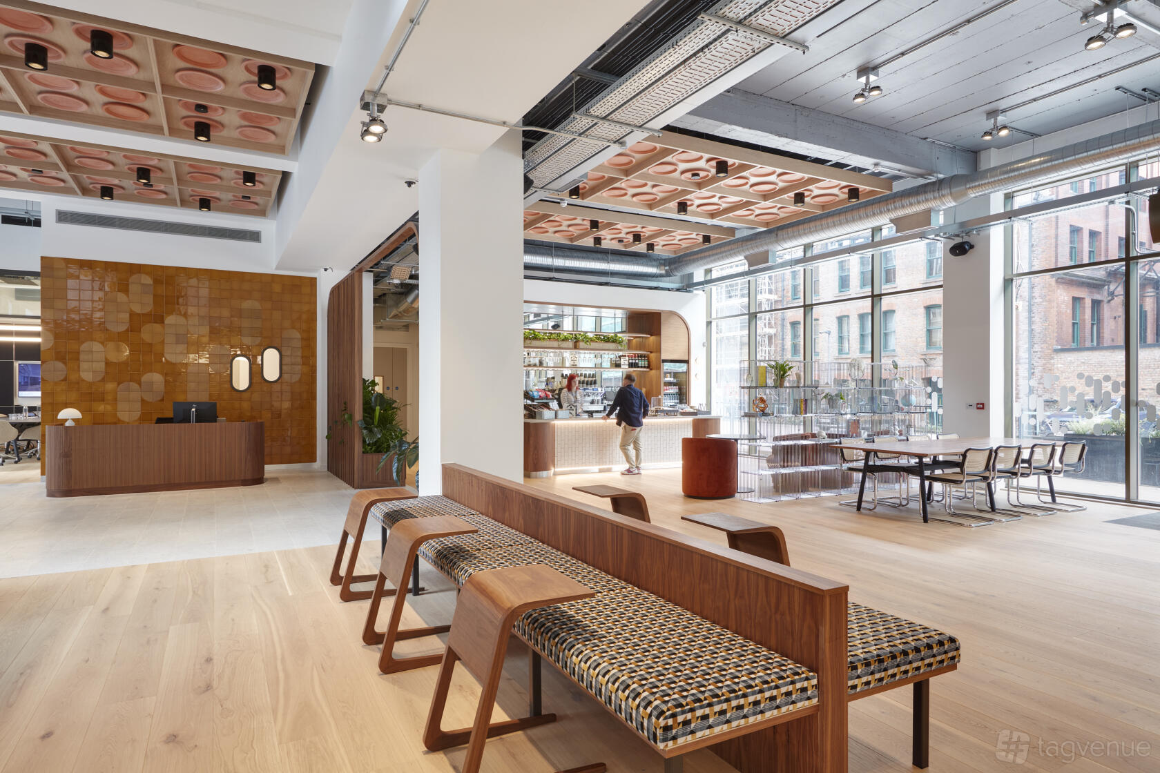 A coworking lounge with patterned benches, wood accents, large windows, and a tiled reception desk at Clockwise Manchester.