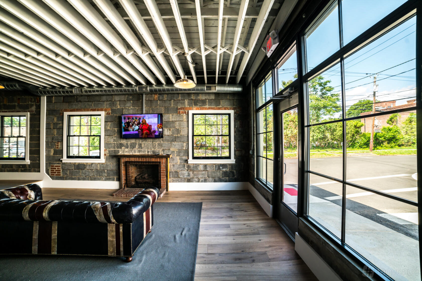 An event venue with exposed beam ceilings, brick walls, large windows, and a leather sofa at 18 Label Studios.