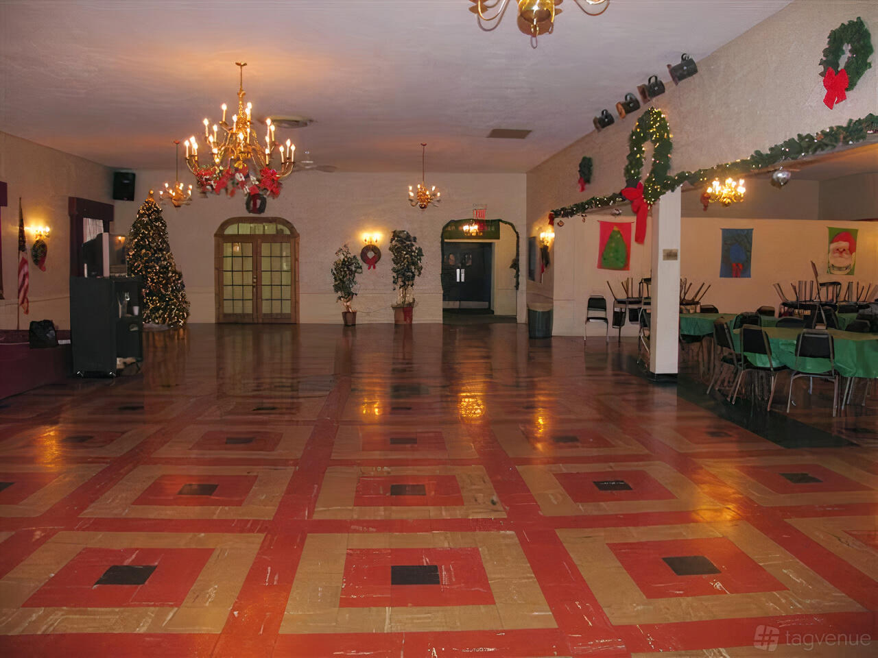 A banqueting hall with polished patterned floors, chandeliers, festive wreaths, and decorated Christmas trees at New Castle County Irish.
