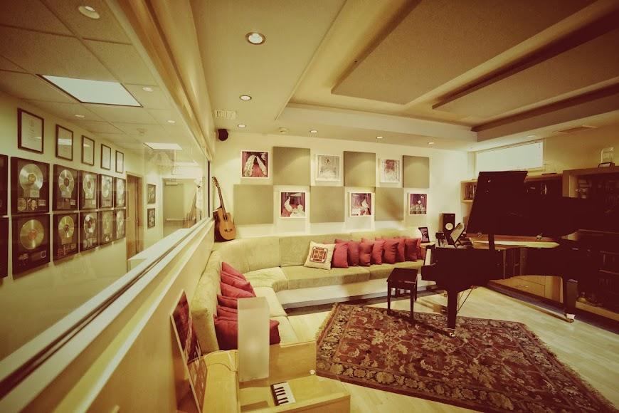 A piano room with a grand piano, sectional sofa, framed music awards, and acoustic panels at Red Dot Recording.