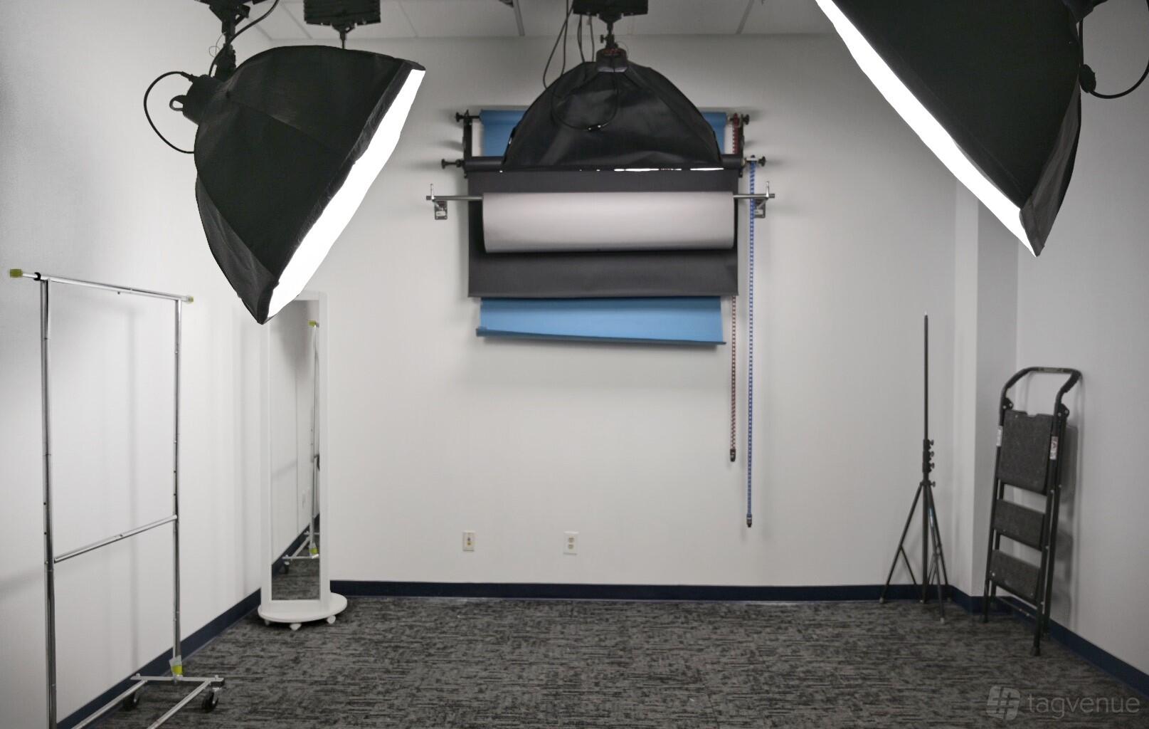 A photo studio with large softbox lights, backdrop rolls, and a rolling clothing rack at Camera Ready Studios.