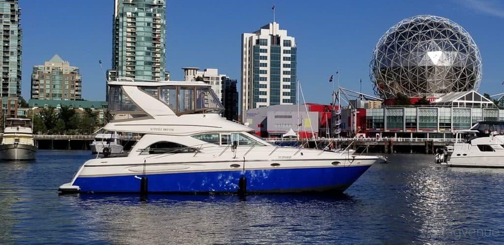 A two-level boat with blue and white exterior docked on the water in front of city buildings at Burrard Queen.