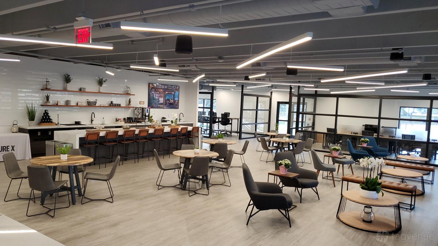 A coworking lounge with round wooden tables, bar seating, and potted plants at Venture X Palmetto Bay.