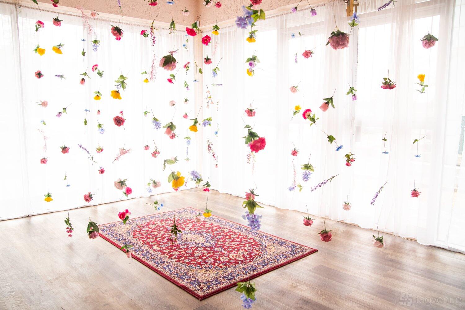 A photo studio with sheer white curtains, hanging floral arrangements, and a patterned rug at Vision Room Studios.