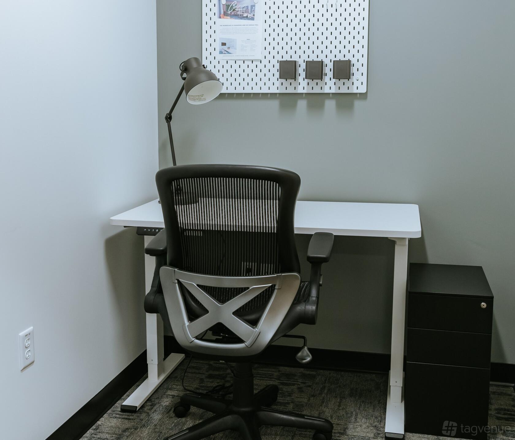 A private office with a modern desk, ergonomic chair, desk lamp, and wall organizer at Common Good Co.