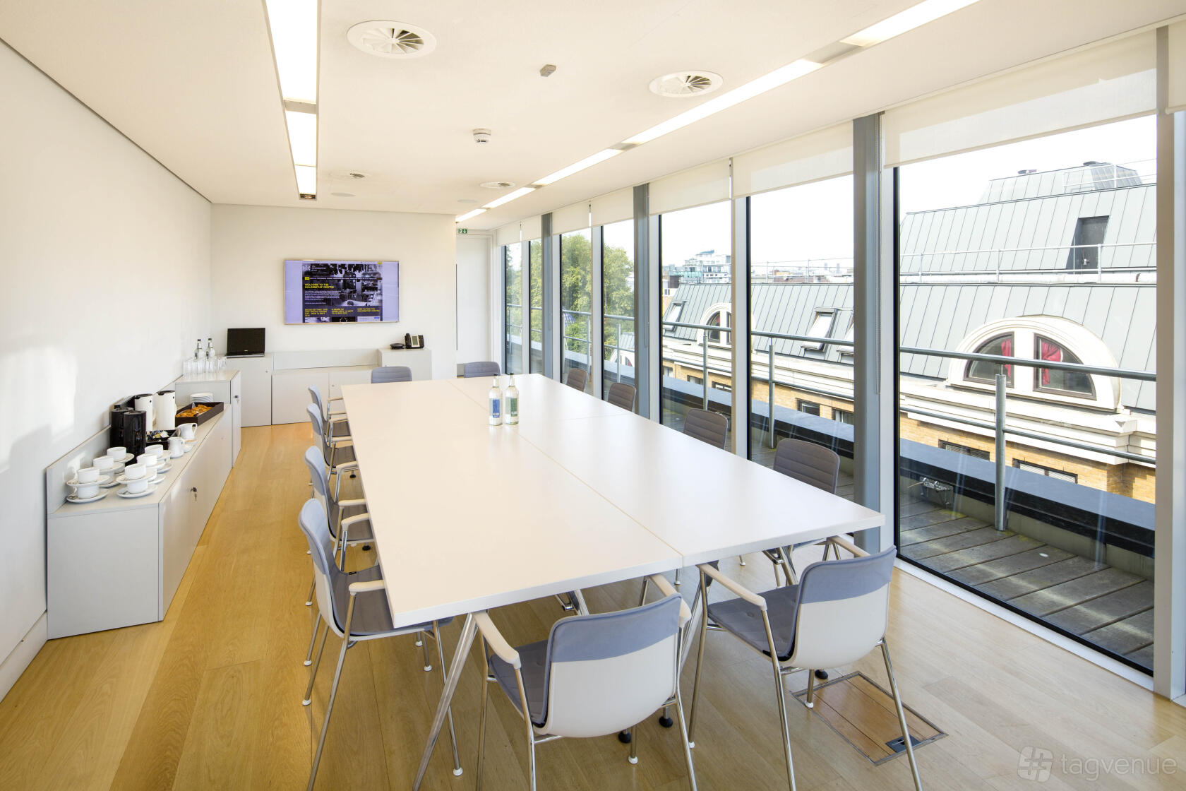 A boardroom with floor-to-ceiling windows, a long white table, and views of rooftops at The Goldsmiths' Centre.