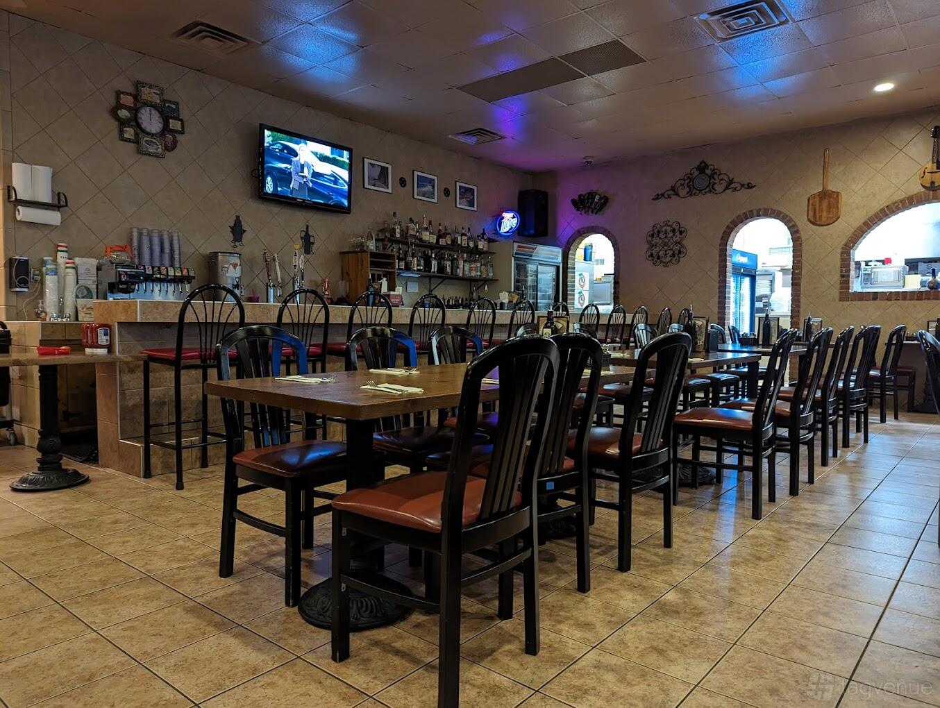 A restaurant dining area with long wooden tables, black chairs, tiled floors, and a bar at Mazzellas Italian Restaurant.