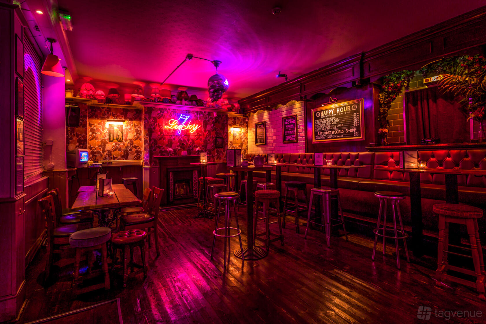 A cocktail bar with neon lighting, vintage wallpaper, high tables with stools, and wooden floors at Simmons | Soho.