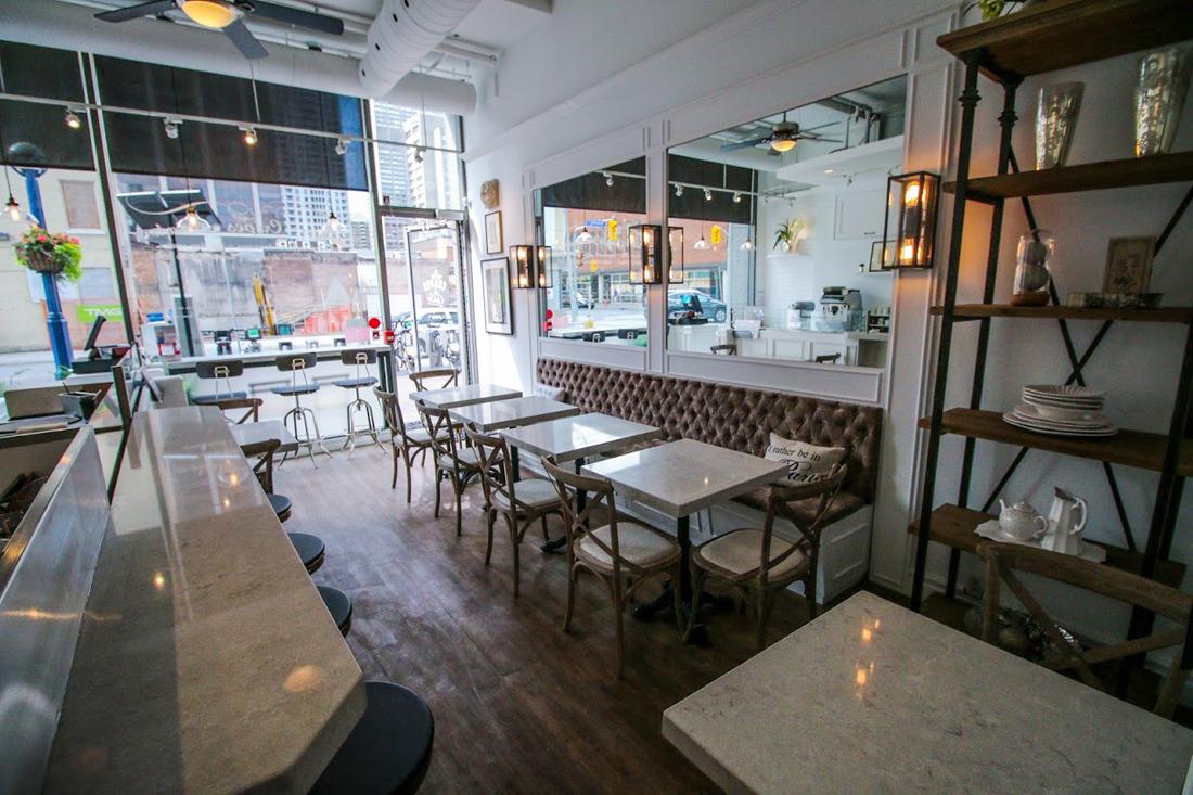 A restaurant featuring marble tables, tufted banquette seating, and large windows at Yorkville Crepes.