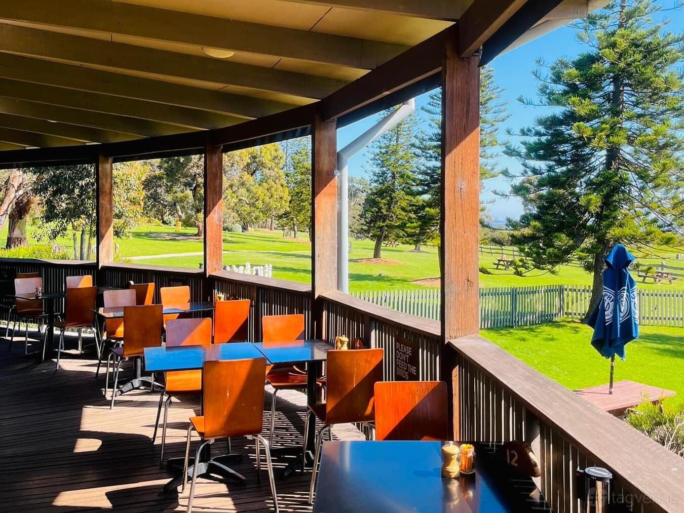 An outdoor event venue with wooden decking, square tables, and views of lawns and trees at Churchill Island.