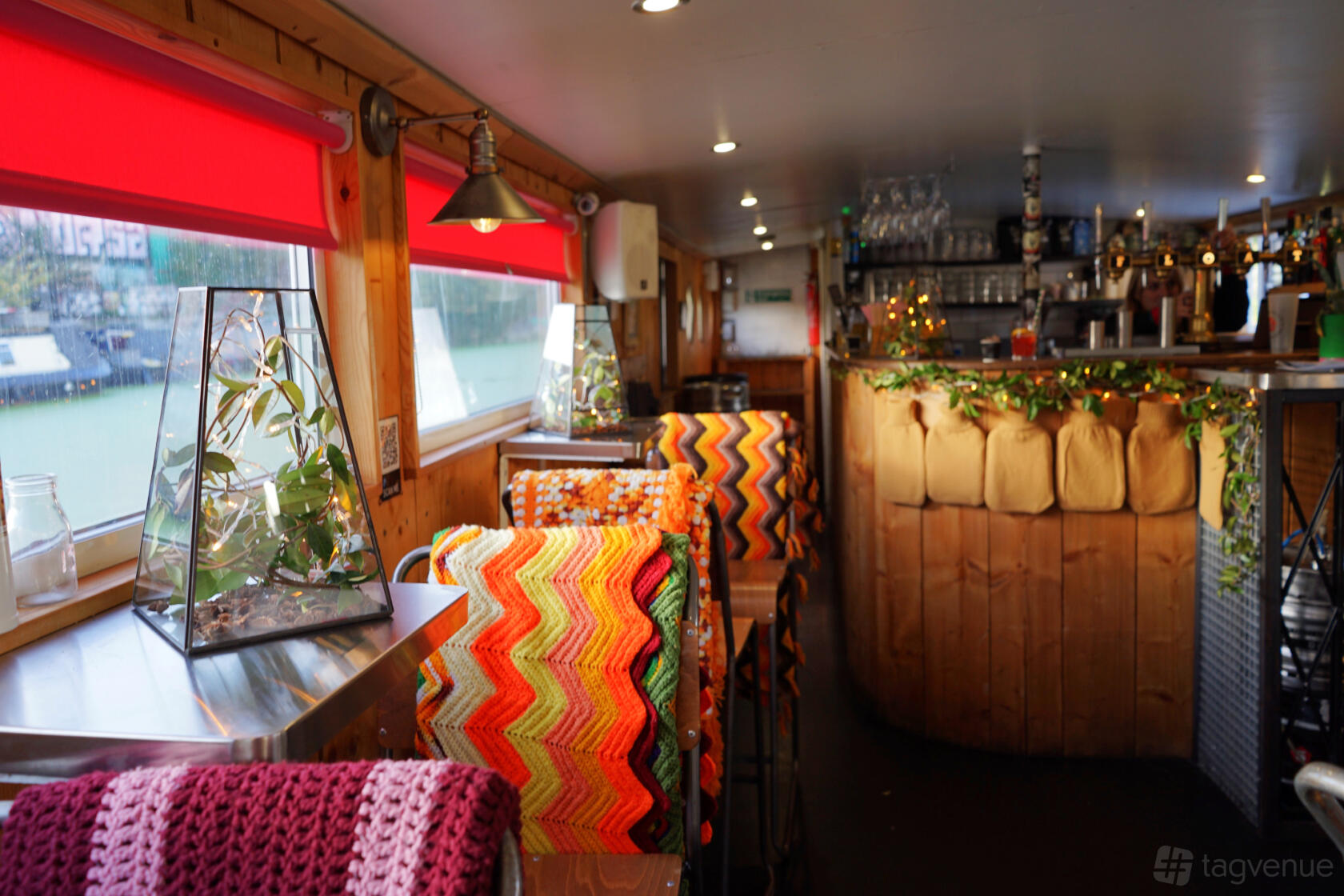 An event space in a bar with wood paneling, colorful crocheted chair covers, and a glass terrarium at The Milk Float.