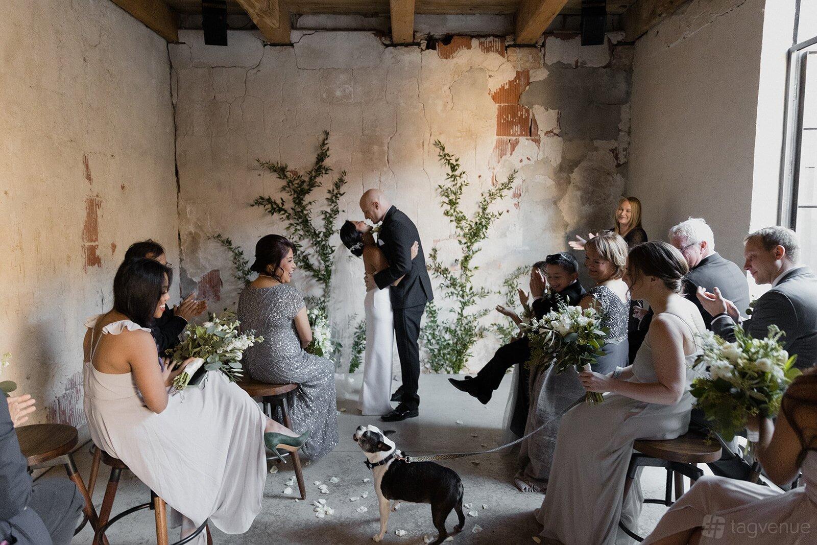A warehouse with textured concrete walls, exposed ceiling beams, wooden stools, and greenery at Charcoal Factory Loft.