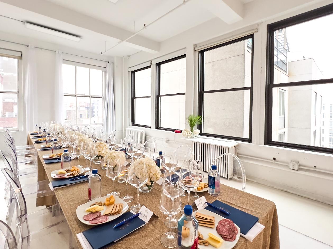 An event venue with large windows, clear chairs, a long table set with plates, bottled water, and floral centerpieces at Event Venue NYC Manhattan 22nd Floor.