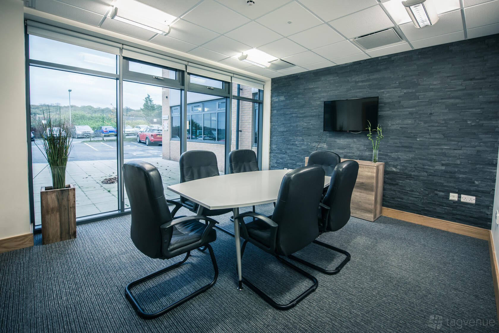 A boardroom with a rectangular table, six leather chairs, floor-to-ceiling windows, and a mounted TV at Hope Park Workspaces, City Gateway.