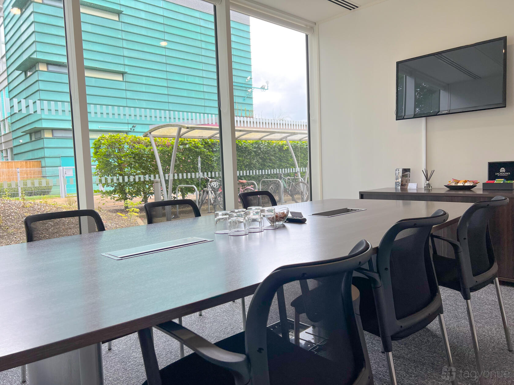 A meeting room with a long wooden table, black chairs, large windows, and a wall-mounted screen at Landmark: Green Park, Reading.
