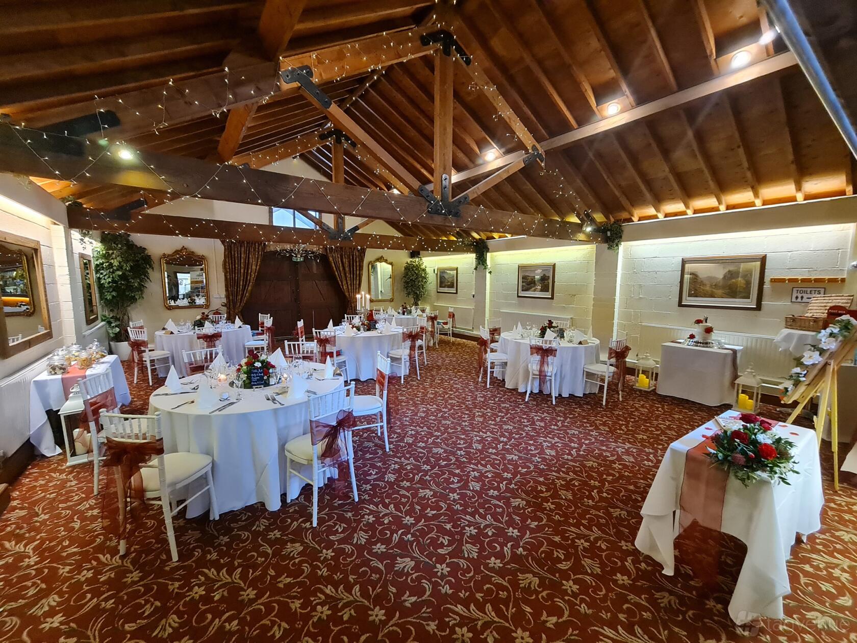 An event space with exposed wooden beams, round tables with white linens, and floral centerpieces at Royal Arms Hotel.