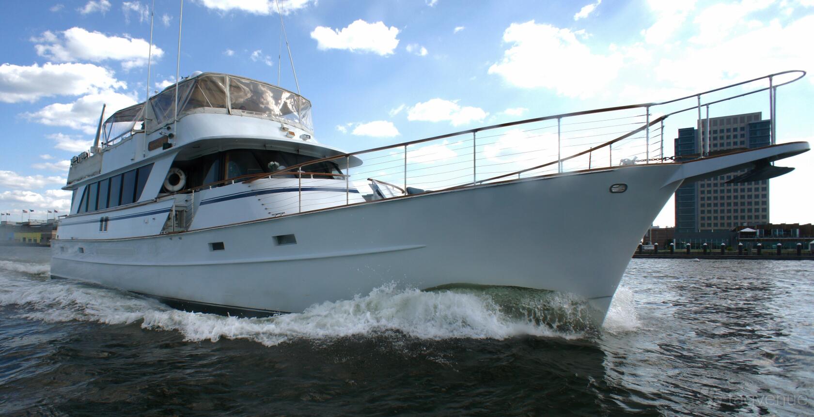 A motor yacht with a covered upper deck and wood railings cruising near a city dock at Del Rio Yacht Charter.