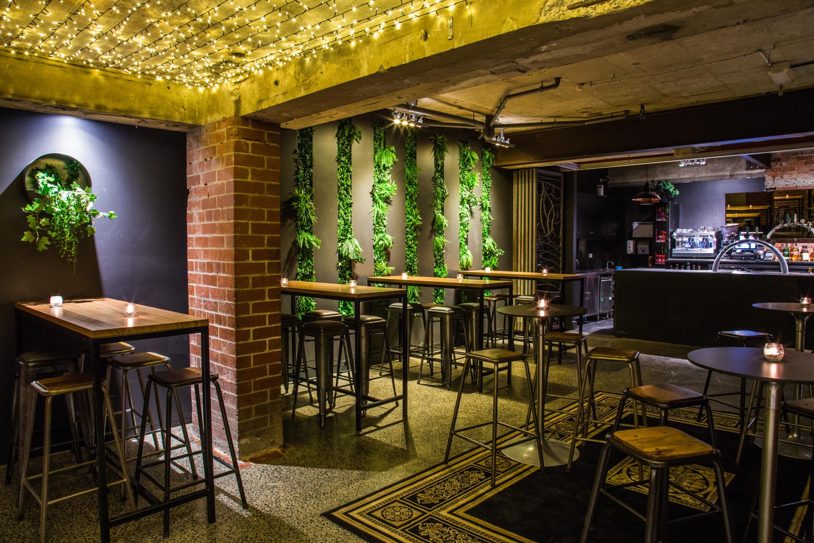 An event space in a restaurant with greenery wall accents, exposed brick, and string lights at MPD Caulfield.