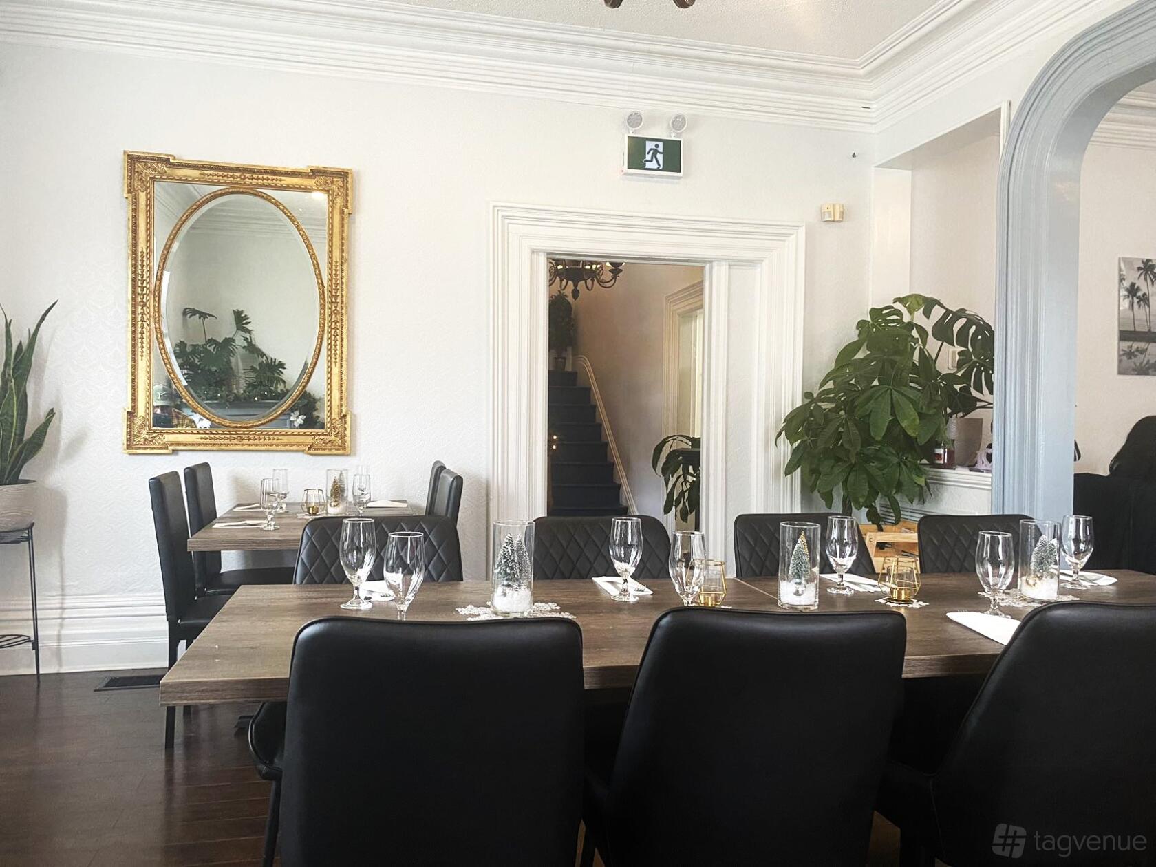 An event space with two long wooden tables, black chairs, and a gold-framed mirror at Laz Authentic Cuisine Inc.