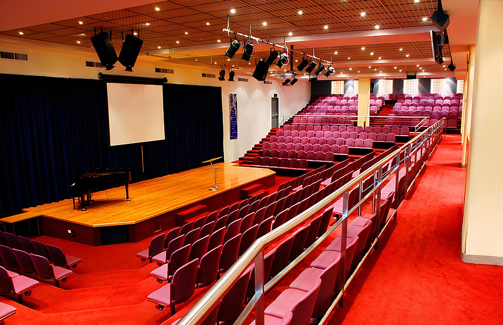 An auditorium with tiered purple seating, a wooden stage, and projector screen at Melbourne City Conference Centre.