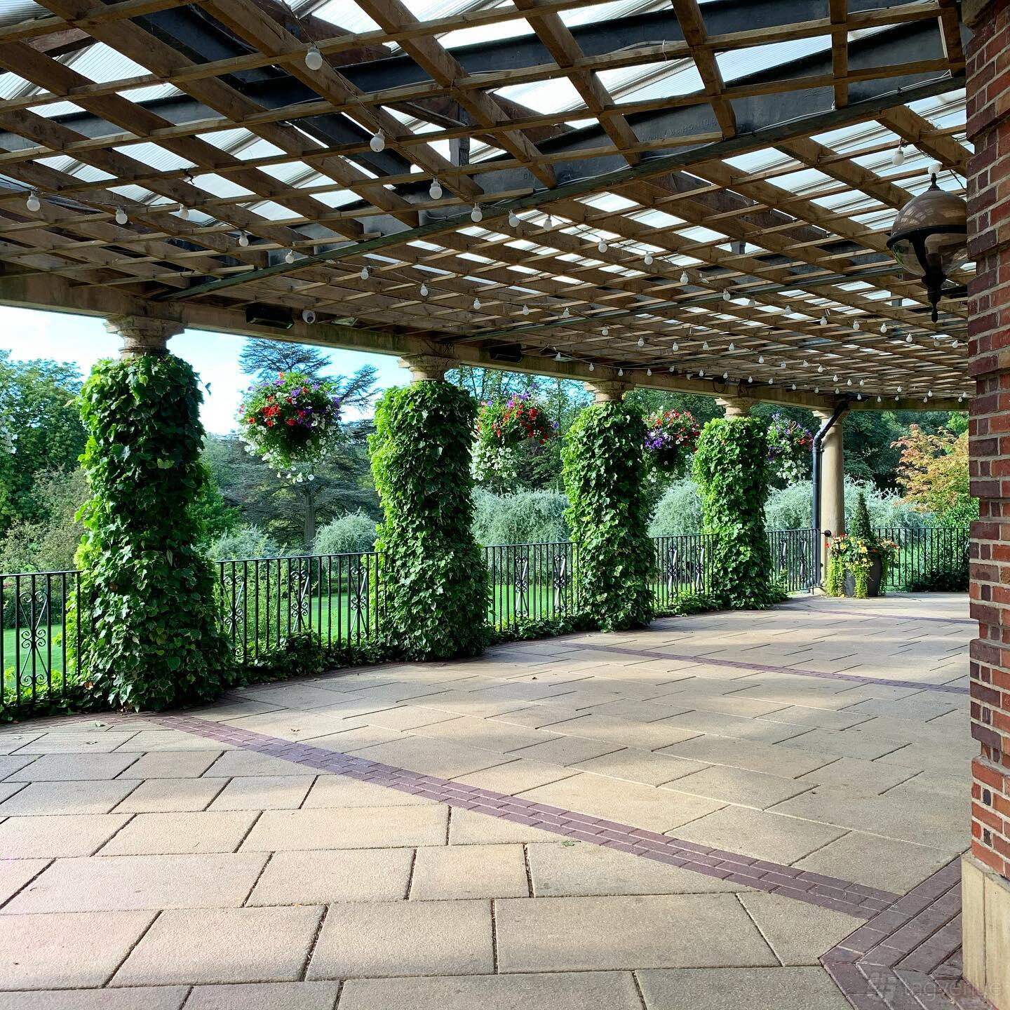 An outdoor event venue with ivy-covered columns and a wooden pergola overlooking landscaped gardens at The Sun Pavilion.