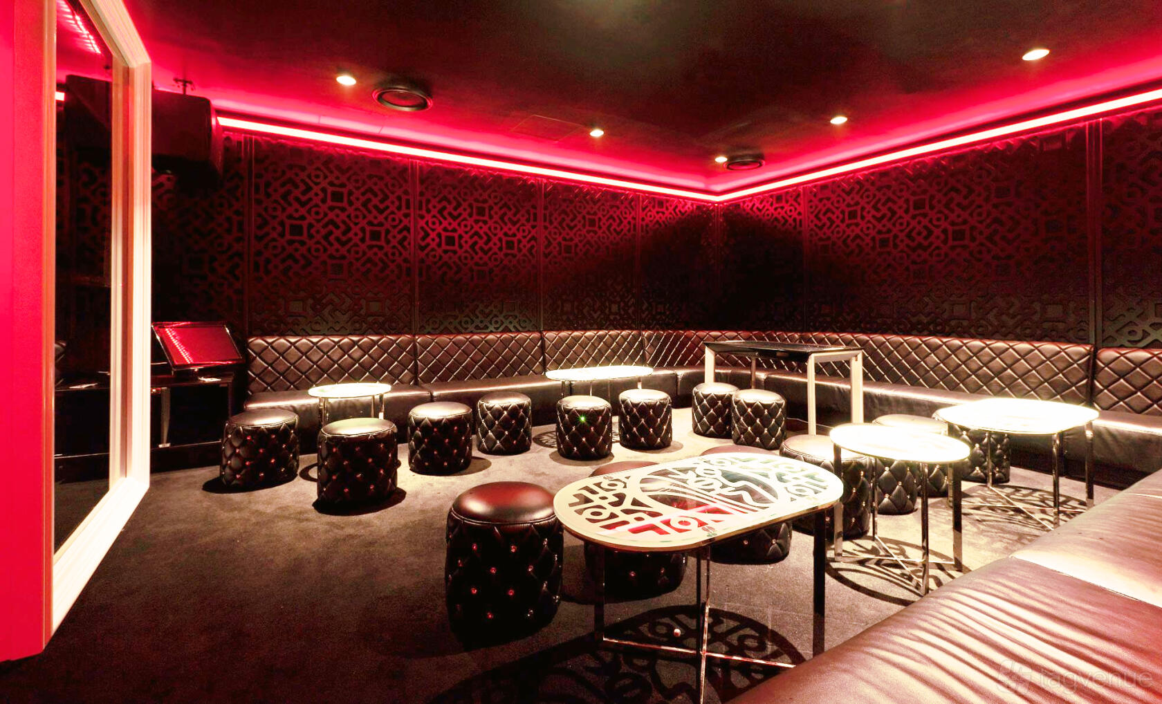 A karaoke event space with tufted black leather seating, small round tables, and red LED lighting at Dynasty Karaoke.