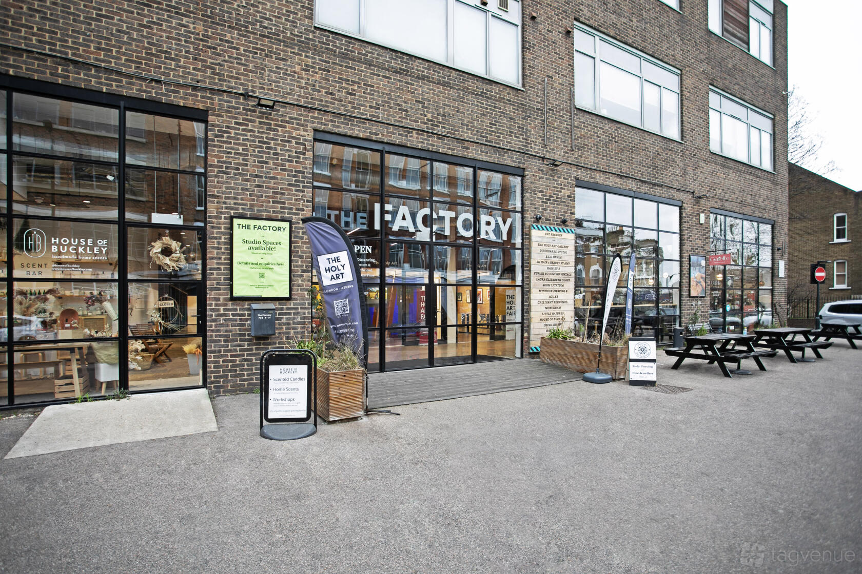 A brick versatile event space with large glass windows, outdoor picnic tables, and signage at The Factory.