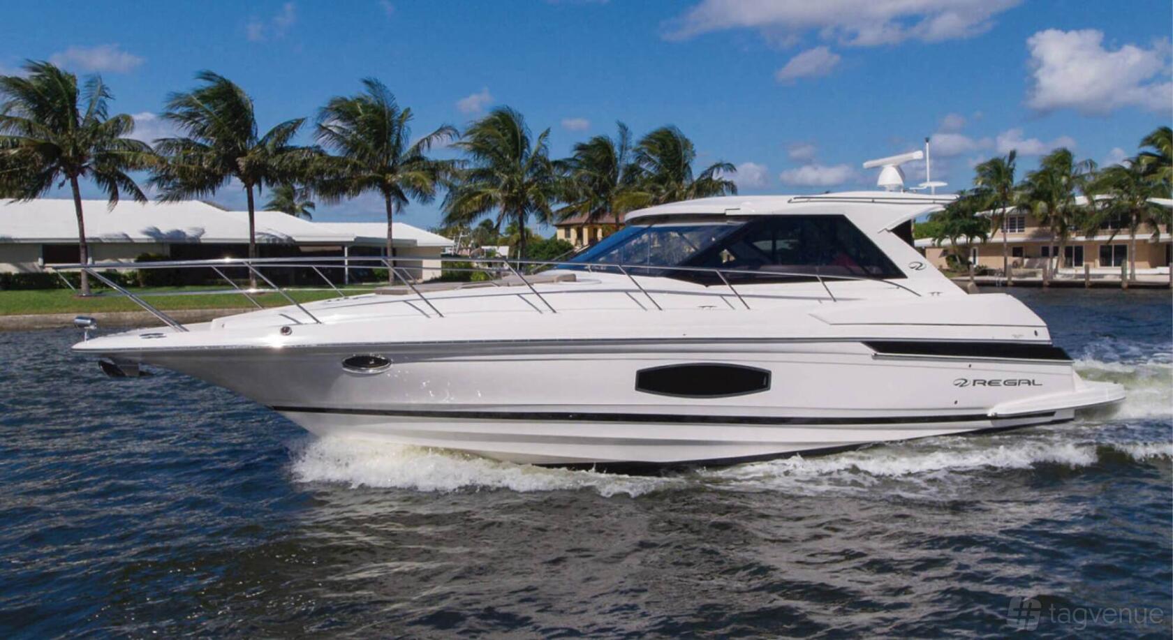 A sleek white yacht cruising on open water with palm trees and houses in the background at Pearl Yacht Charters.