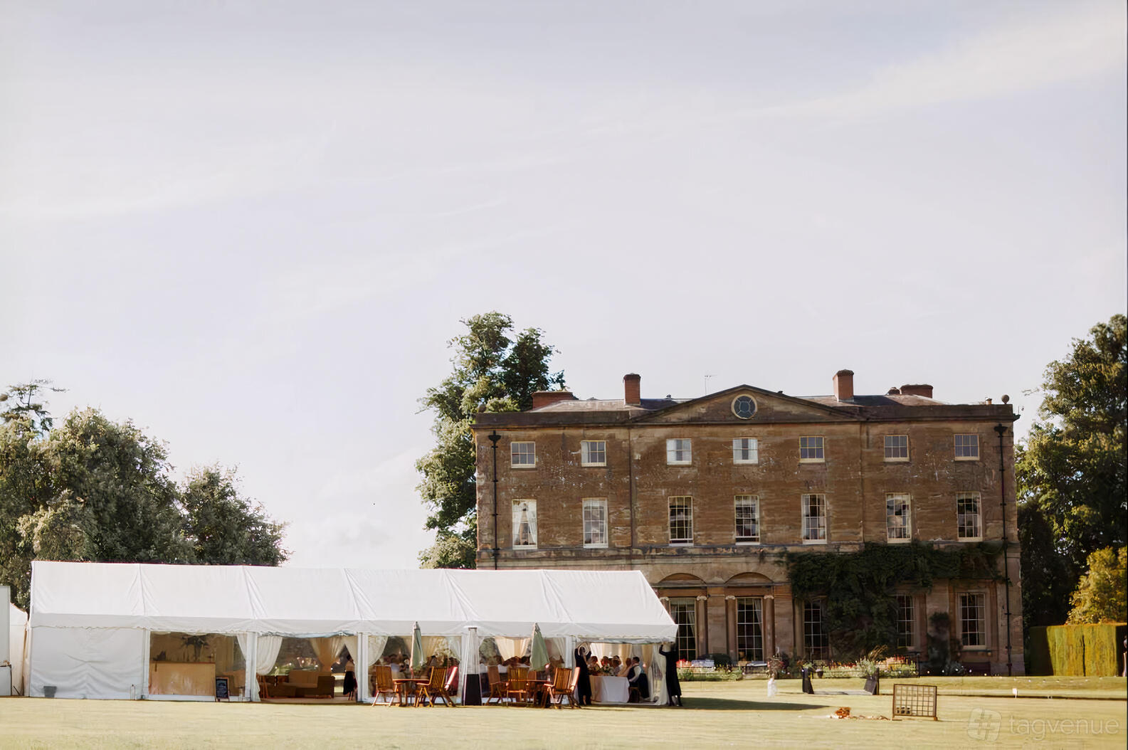 A country house with a large white marquee, outdoor seating, and Georgian architecture at Courteenhall Estate.