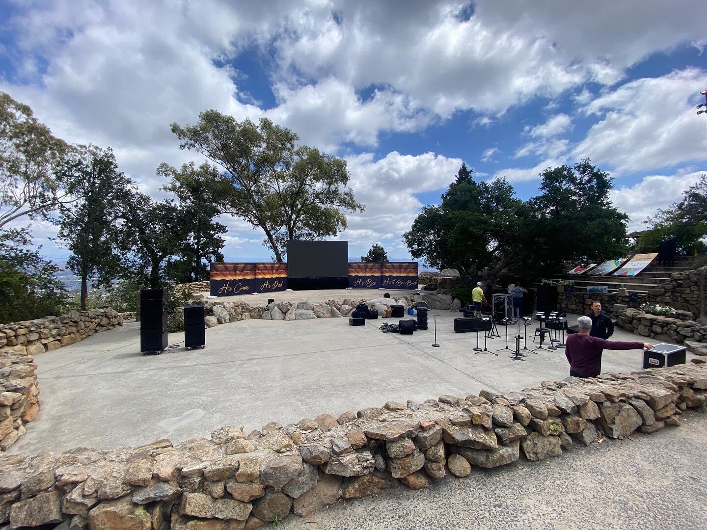 An outdoor event venue with a stone wall enclosure, stage, and sound equipment setup at Mt. Helix Park.