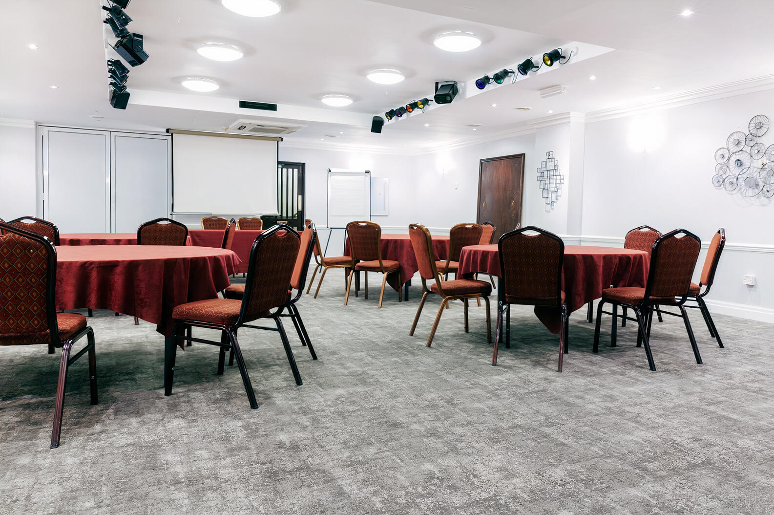 A meeting room with round tables covered in red linens, cushioned chairs, and a ceiling-mounted projector at Best Western Bradford Guide Post Hotel.