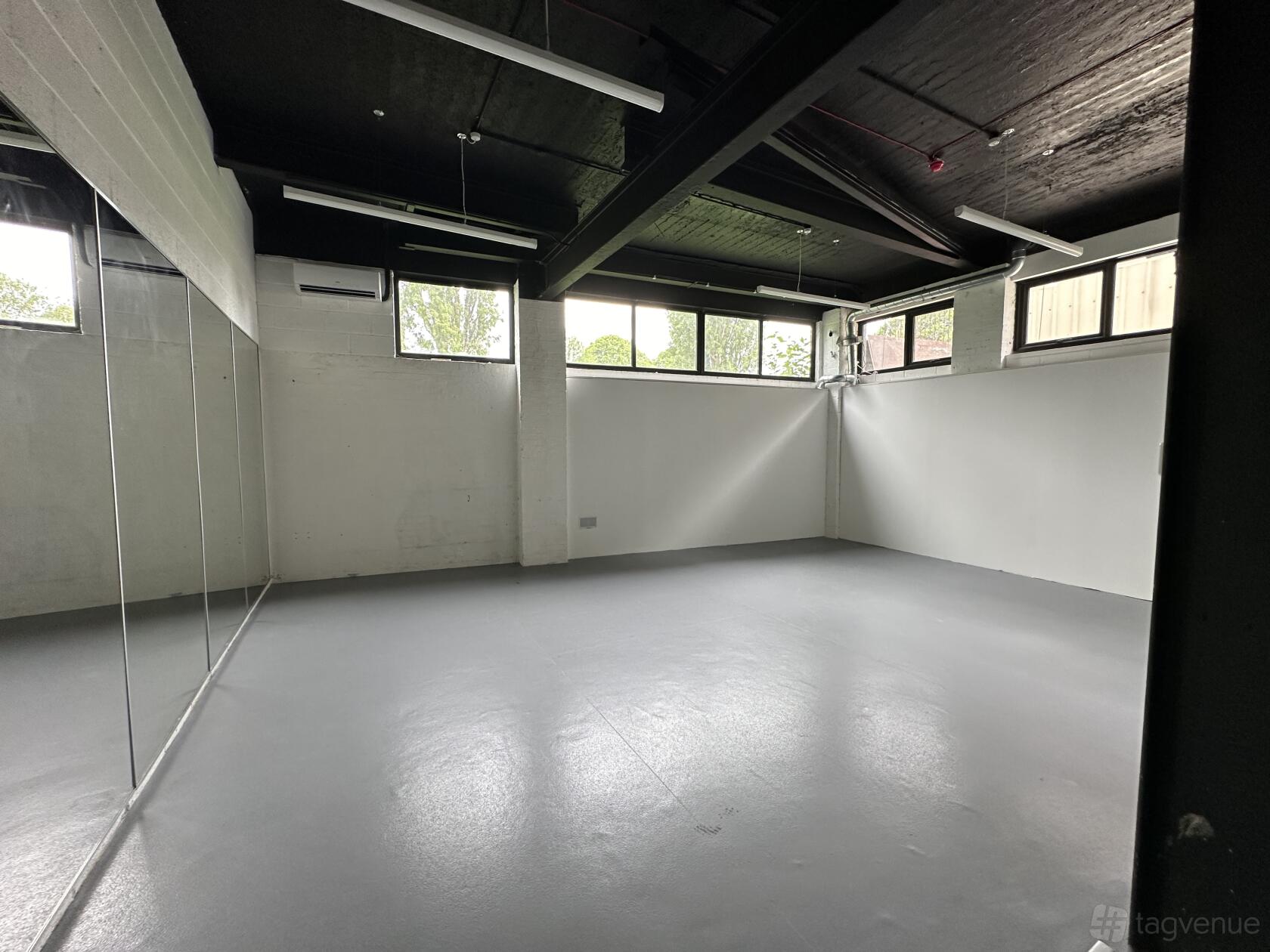 A dance studio with mirrored walls, gray flooring, and large windows at Cobbold Works.