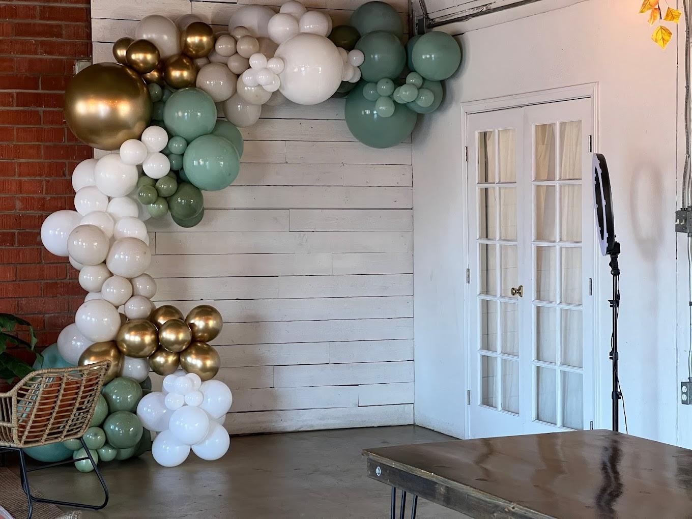 A warehouse event space with a balloon arch, red brick wall, white wood paneling, and French doors at Brick + Laurel.