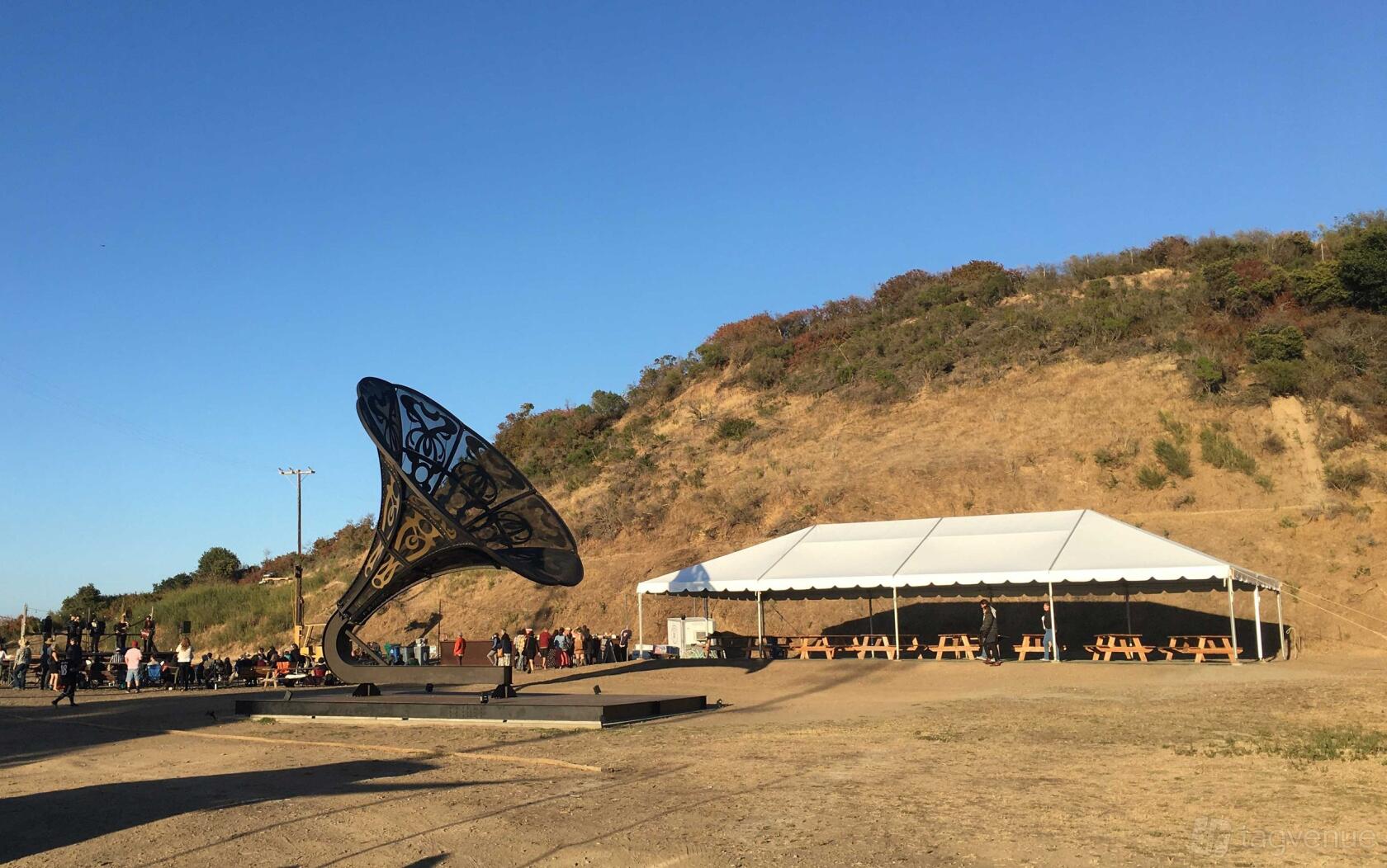 An event venue with a large white tent and picnic tables set on gravel beside a hillside at Point San Pablo Harbor.