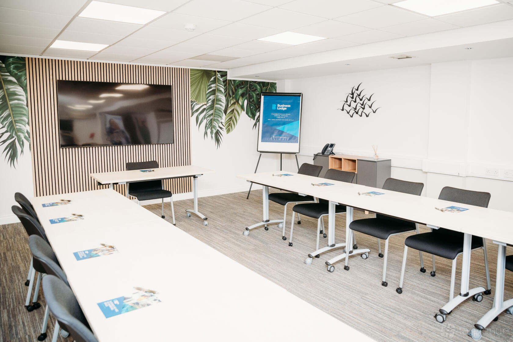 A meeting centre with U-shaped tables, a large wall-mounted screen, and tropical leaf wall decor at BusinessLodge.