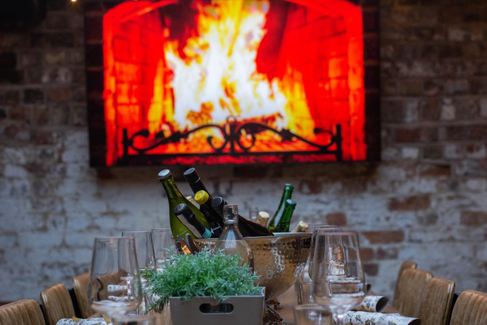 A dining room with exposed brick walls, a digital fireplace display, and a long table set with wine at Duke Street Market.