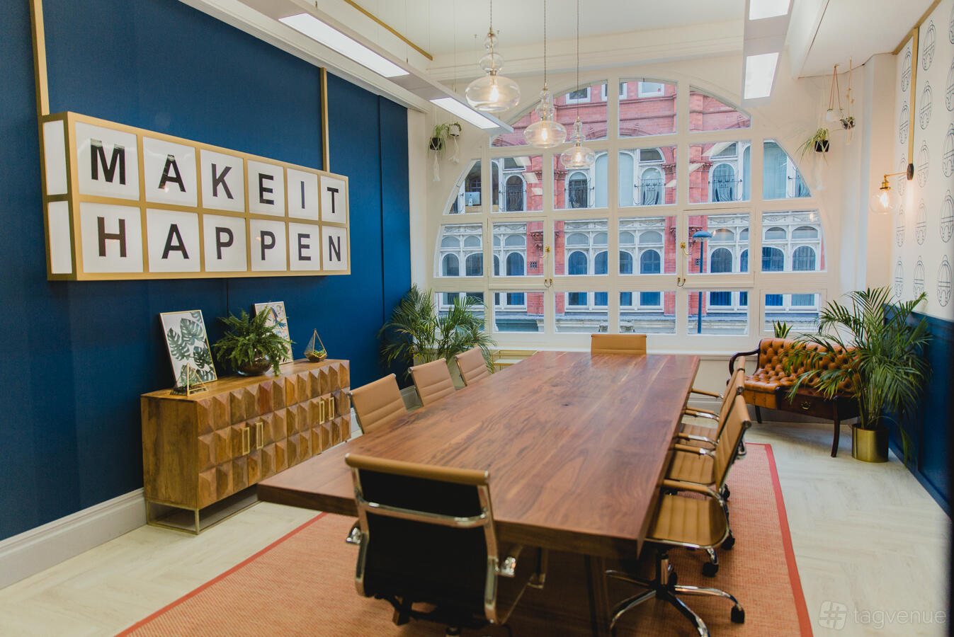 A meeting room with a large wooden table, leather chairs, decorative blue wall, and large arched windows at Wizu Workspace - Leeds - Leeming Building.