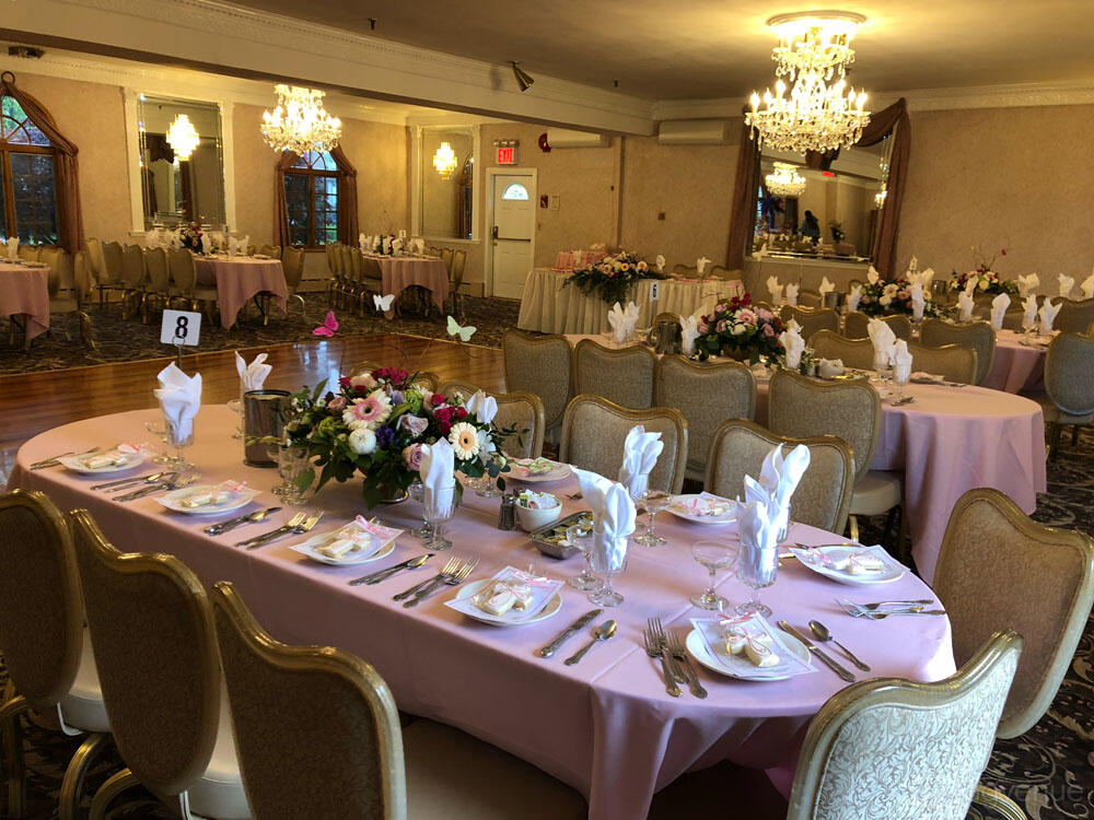 An event venue with chandeliers, round tables draped in pink linens, and floral centerpieces at The Crystal Room.
