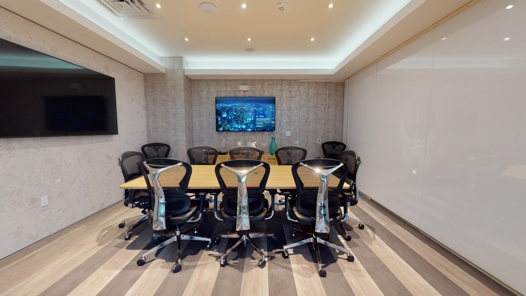 A meeting room with a long wooden conference table, mesh chairs, and a wall-mounted display at Iconic Workspaces @ Aventura.