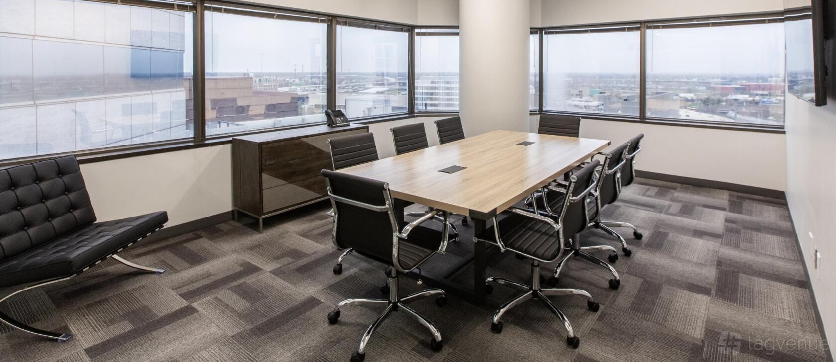 A meeting room with a wood conference table, black chairs, and wraparound windows overlooking the city at Lyric Works.