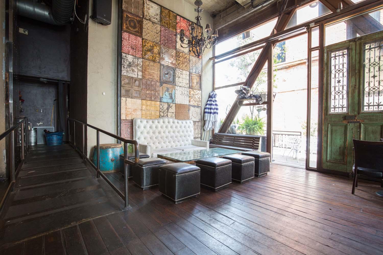 An event space in a bar with a tufted white sofa, black ottomans, chandelier, and floor-to-ceiling windows at Saint Felix Hollywood.