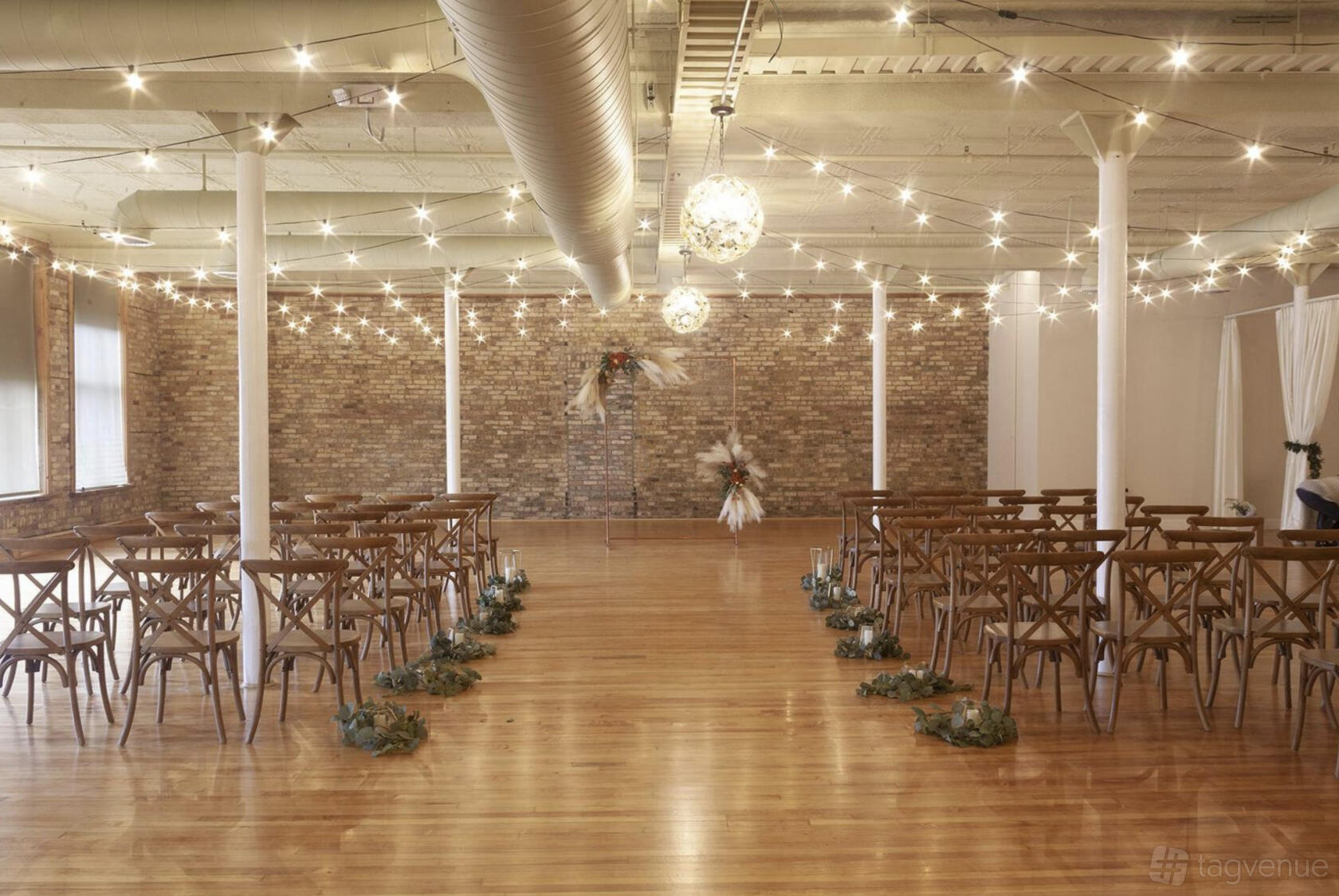 A loft with exposed brick walls, string lights, and wooden chairs arranged for a ceremony at The Highland Loft.