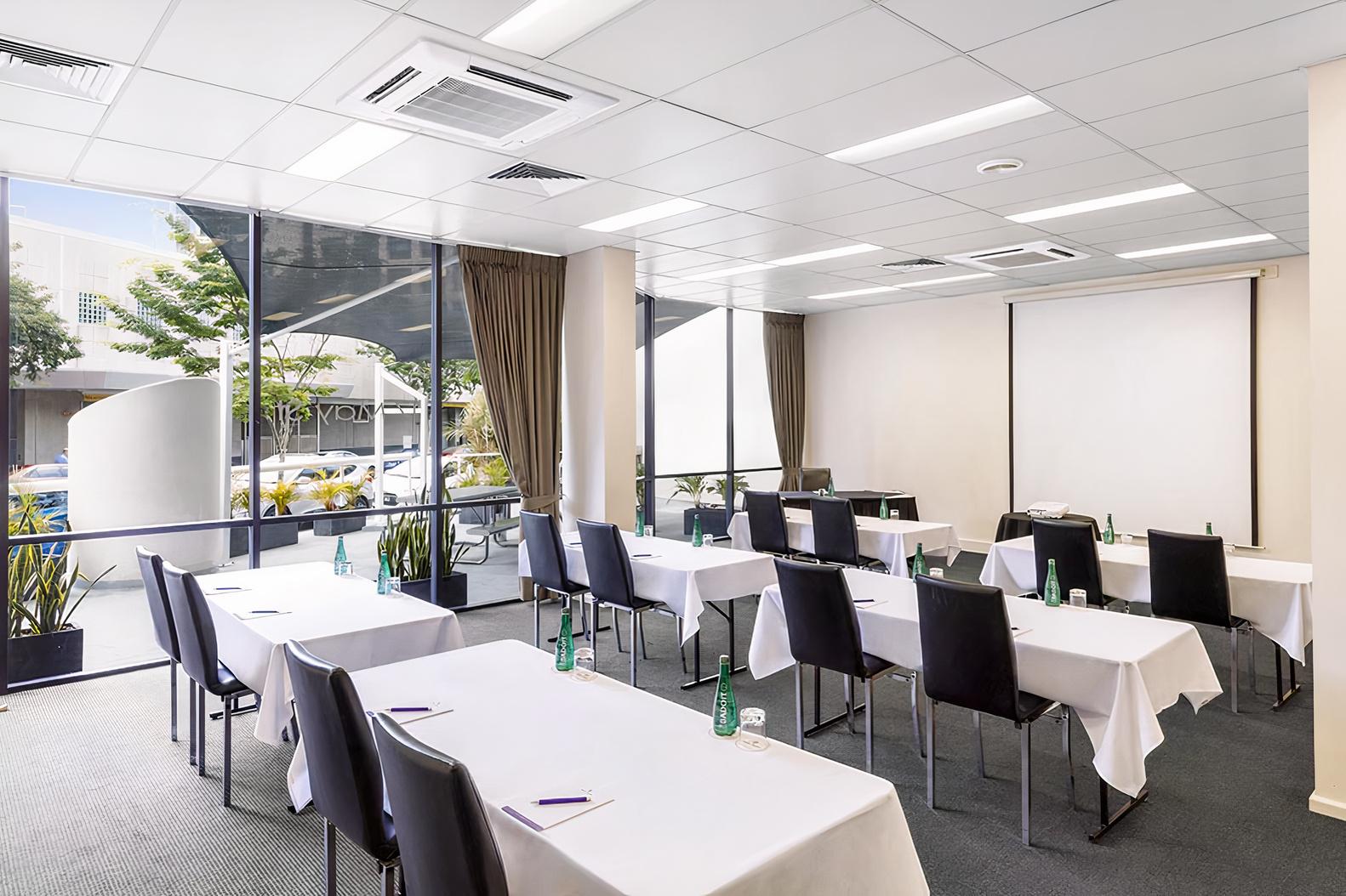A bright meeting room with floor-to-ceiling windows, white tables, and black chairs at Park Regis North Quay.