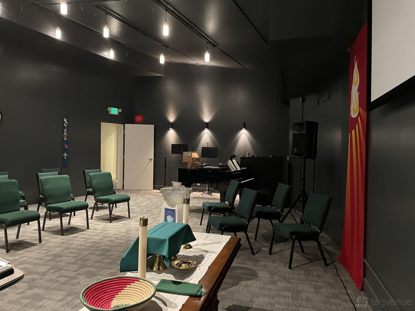 An event space with green cushioned chairs, upright piano, and a baptismal font at Saint Paulus Lutheran Church.