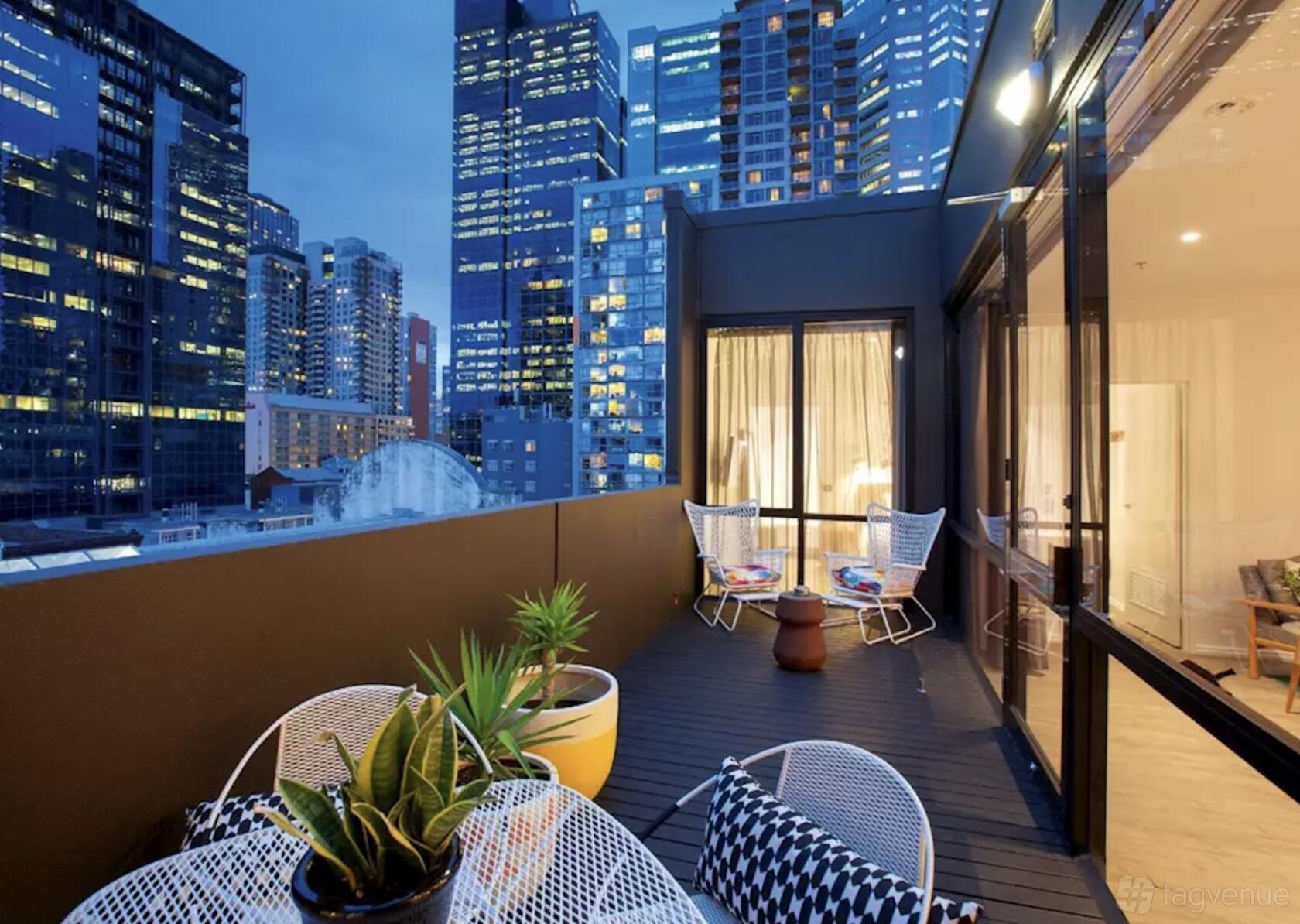 A hotel terrace with potted plants, wire chairs, and views of city skyscrapers at Laneways By Ovolo.