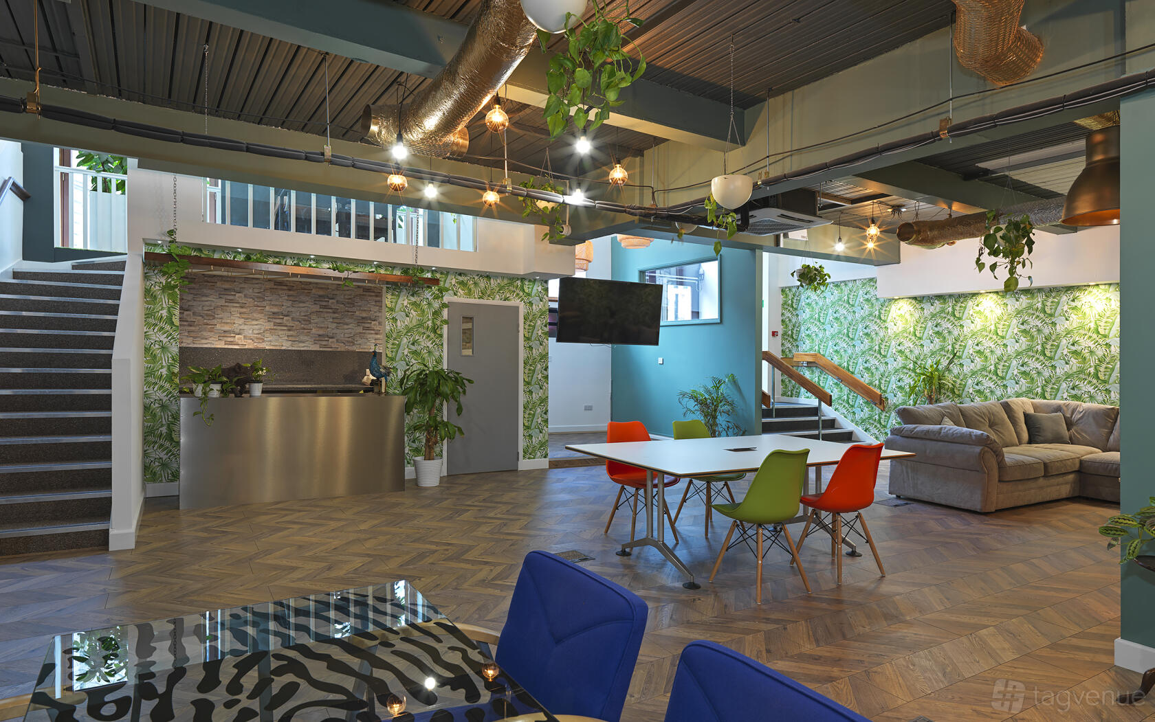 A coworking space with colorful chairs, wood flooring, leafy wallpaper, and lounge seating at Arboretum.