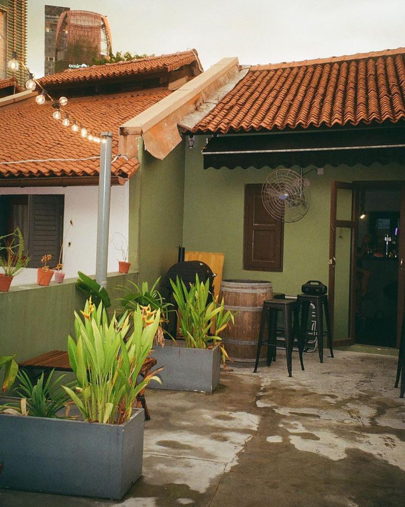 An outdoor pub area with potted plants, barrel tables, bar stools, and string lights at The Otherside.