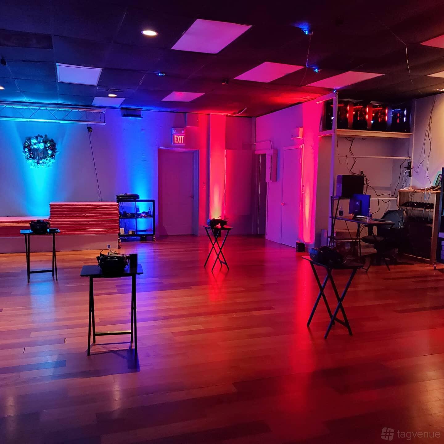 An event venue with VR headset stations, colored LED wall lighting, and wood floors at Key To Amaze VR.