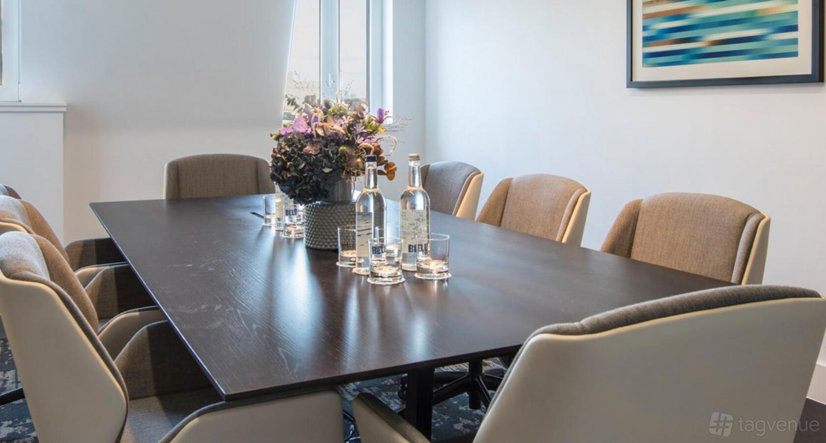 A meeting room with a dark wooden table, upholstered chairs, and bottled water at 20 North Audley Street.
