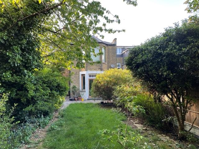 A photo and film studio with an overgrown grassy garden, mature trees, and brick facade at Victorian Flat with overgrown garden.